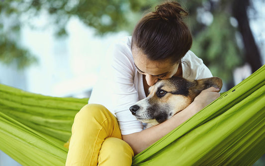 woman sits on a hammock and hugs her dog